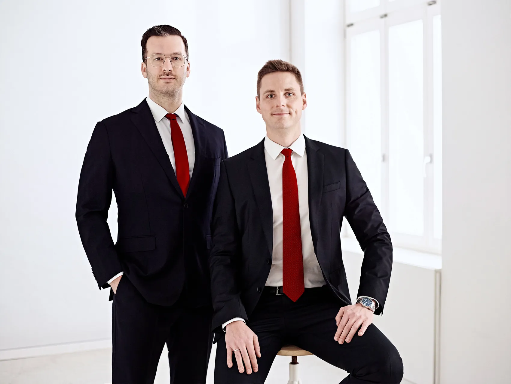 Johannes Schmidt und Deniz Schöne, Gründer und Managing Directors von Schmidt & Schöne, in dunklen Anzügen mit roten Krawatten