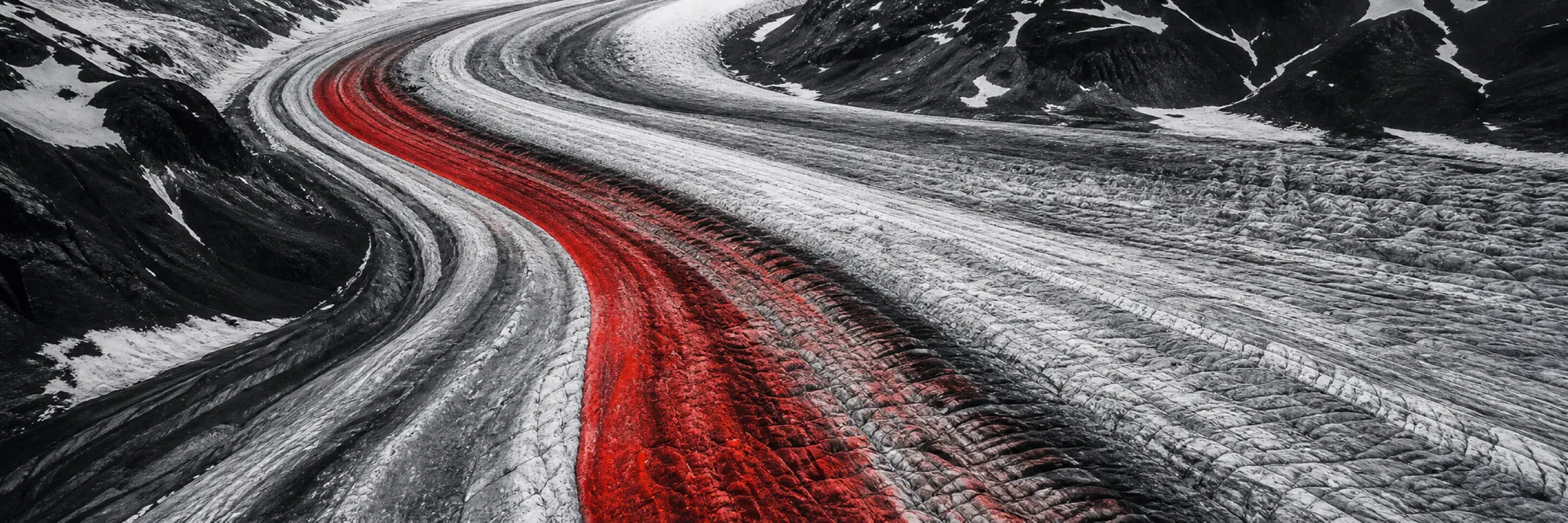 Monochromer Gletscherstrom aus der Luft, die Mittelmoräne zieht als rotes Band durch das Eis